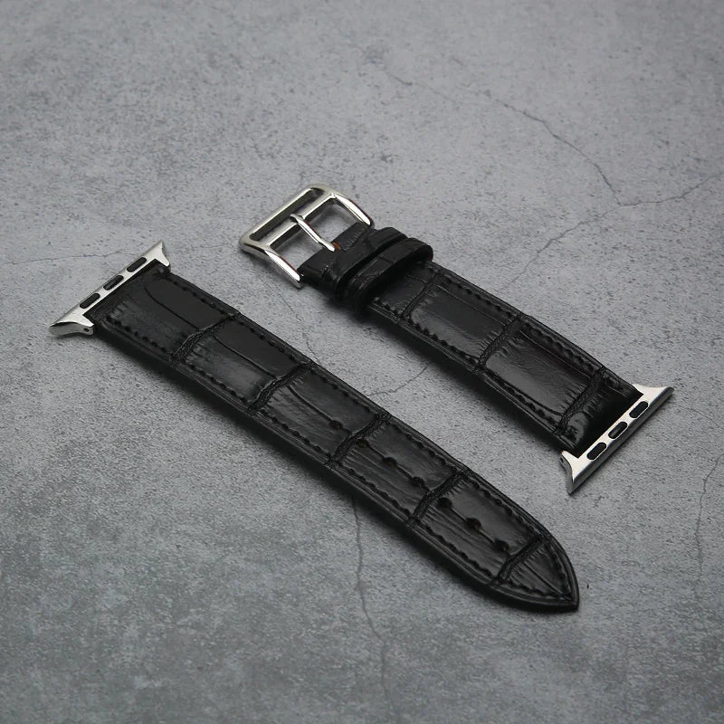 Black aligator leather watch strap with silver buckle on a gray concrete surface