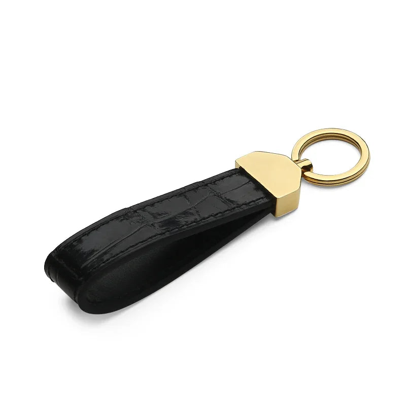 Glossy black crocodile skin keychain with gold accent on a white background