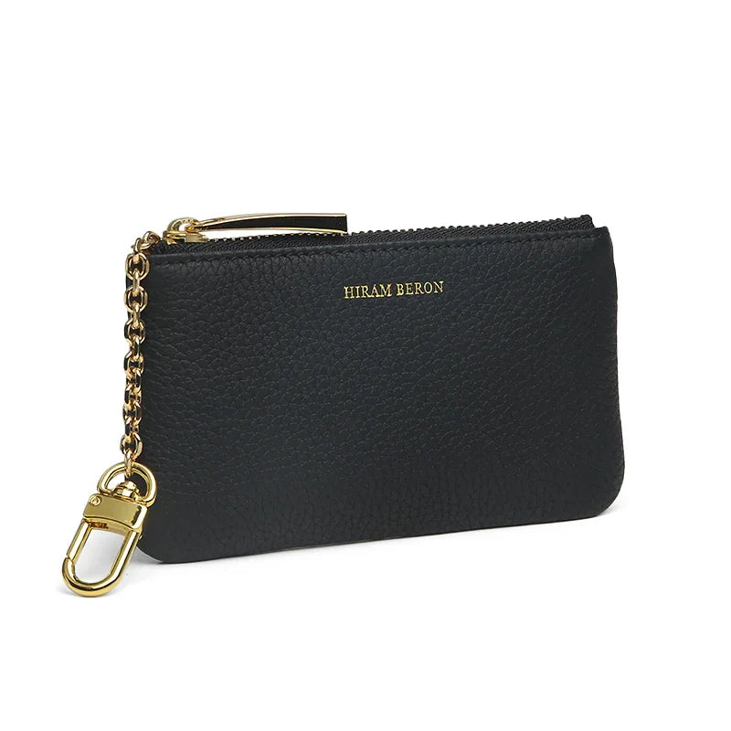 Black pebble leather key case with gold chain and clasp on a white background