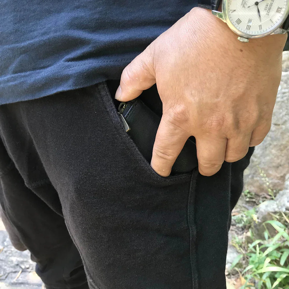 Person wearing black pants with a hand holding a pouch pouch, outdoors.