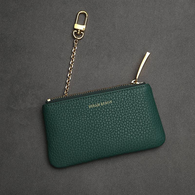 Green leather key case with gold chain and clasp on a gray background