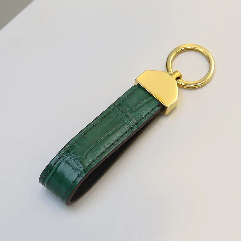 Green crocodile skin keychain with gold accent on a light gray background