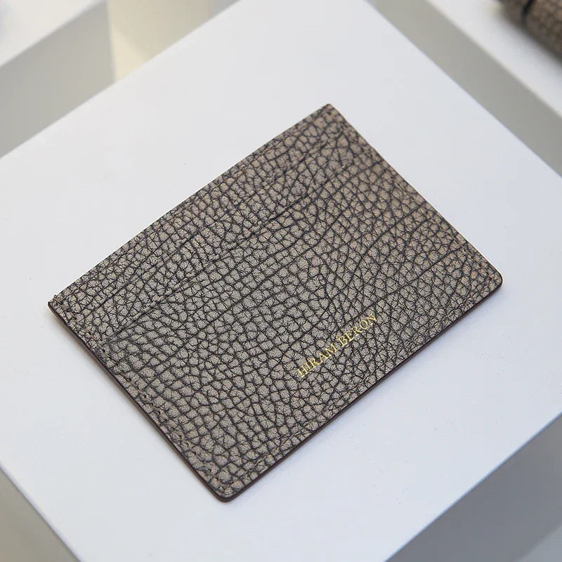 Pebble gray cardholder with 'Hiram Beron' branding on a white surface
