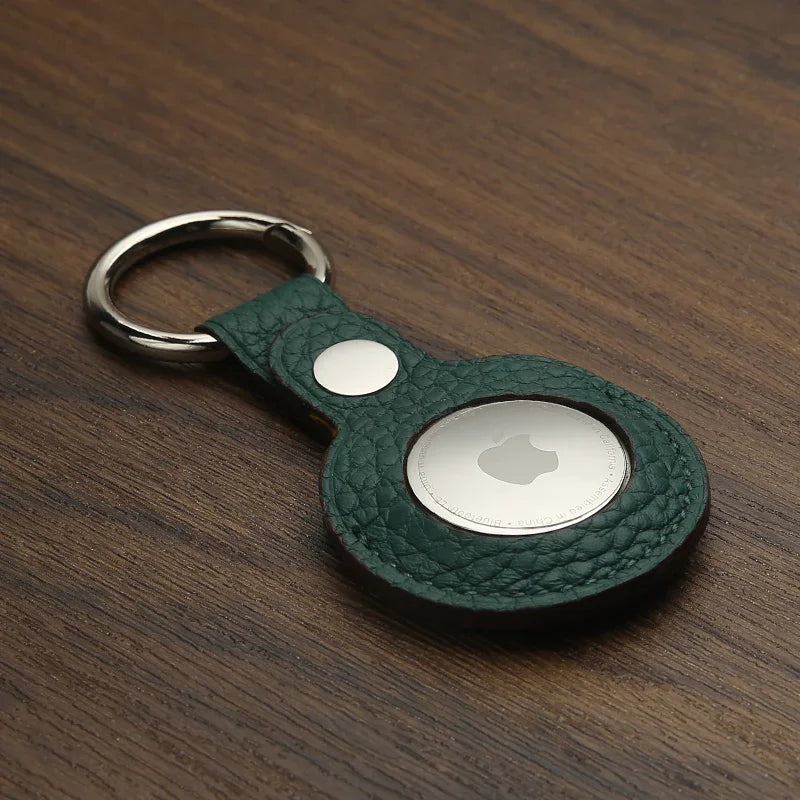 Green pebble leather airtag cover with keychain on a wooden surface