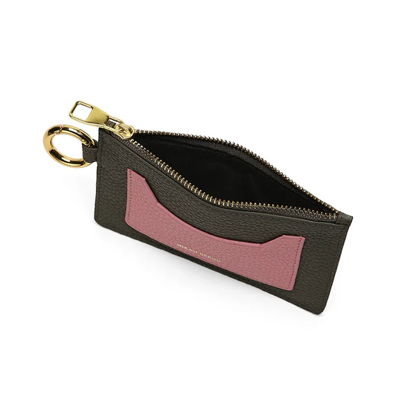 Small dark grey leather card holder with pink card slot outside and with dark grey interior and gold zipper on a white background