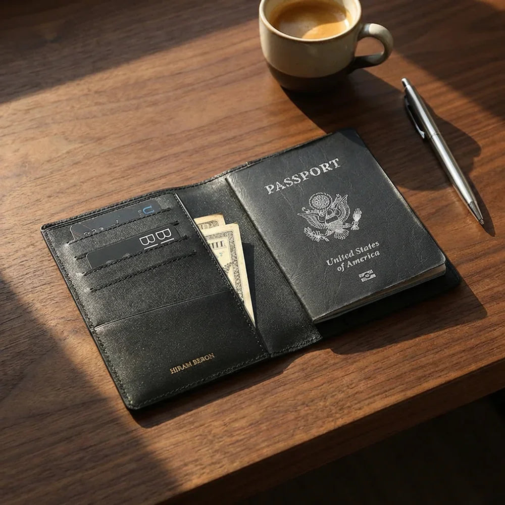 Black leather passport holder with passport holder on a wooden table with a cup of coffee and pen.