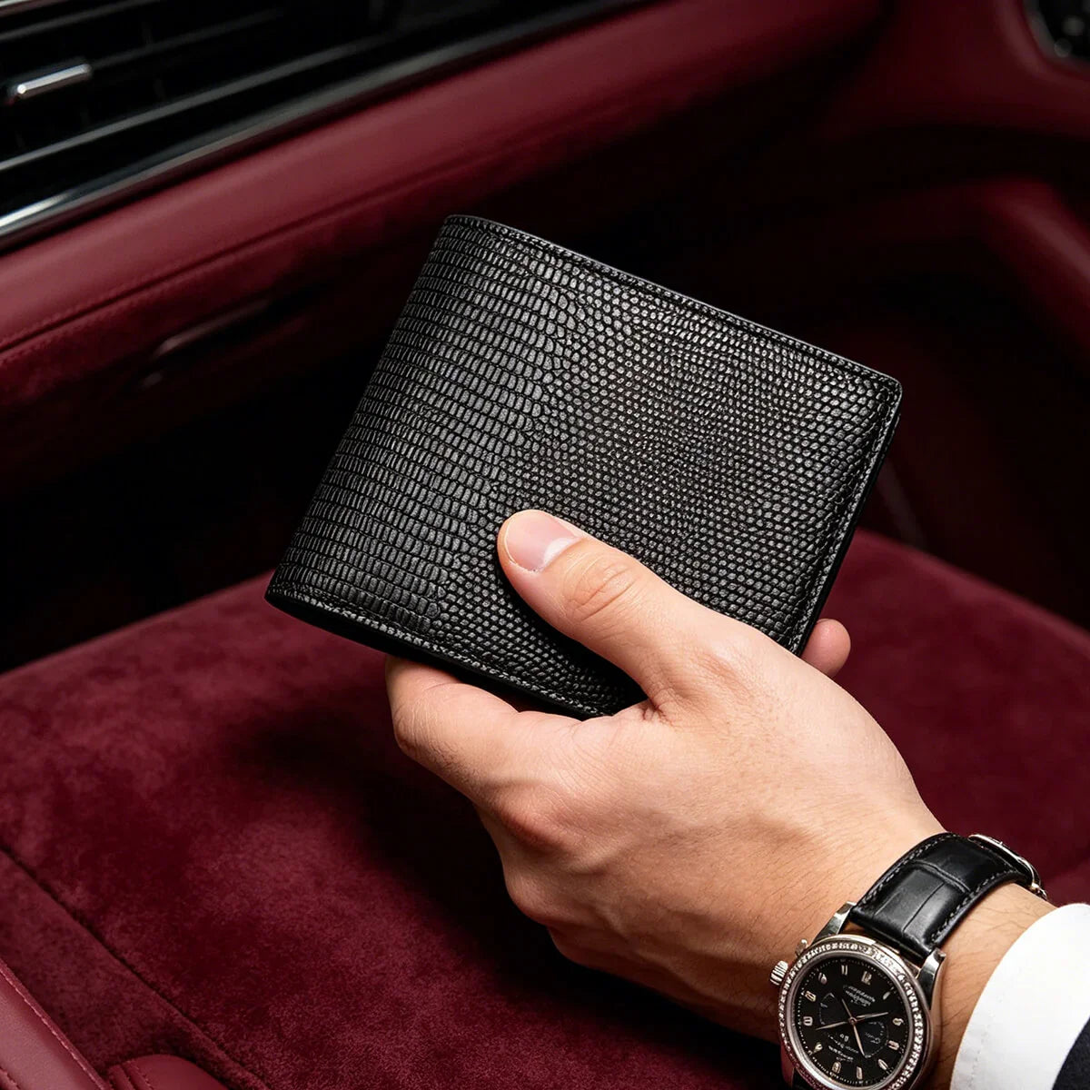 Hand holding a black lizard pattern wallet with a watch on a red interior background