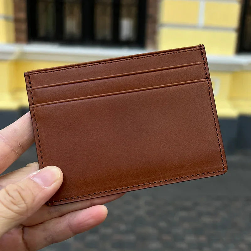 Brown leather cardholder held by a hand with a blurred background