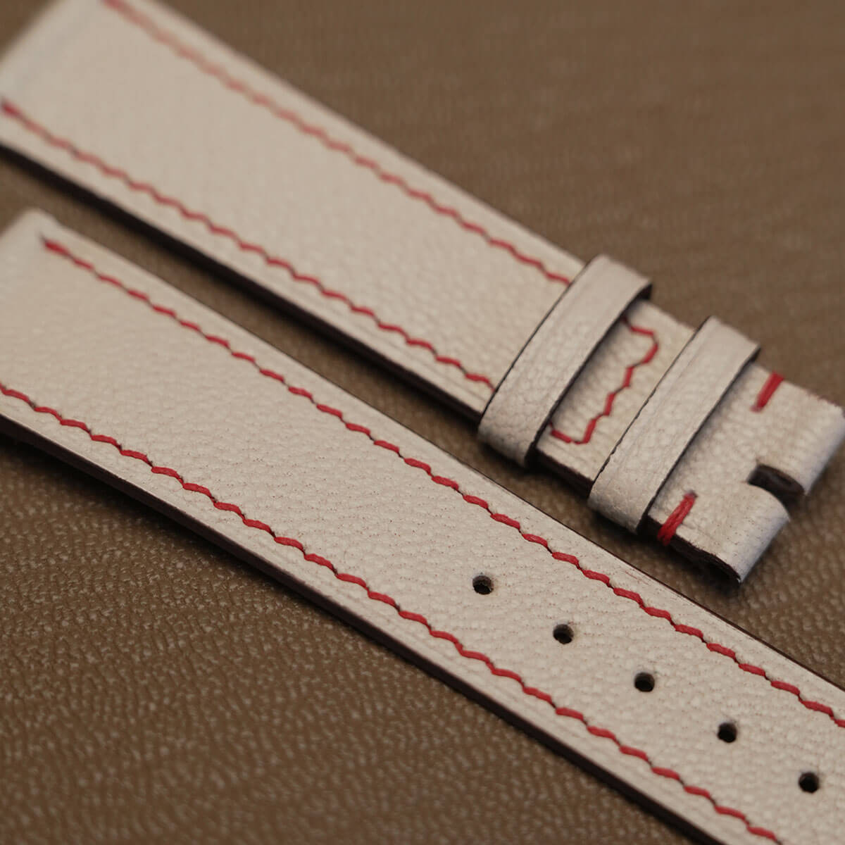Macro texture of French Alran goatskin grain featuring clean red contrast stitching and sealed edge paint