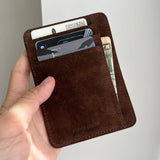 Brown leather wallet with cards and money held by a hand against a light background