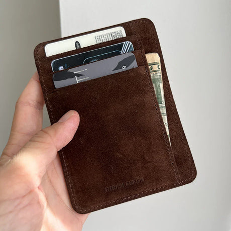 Brown leather wallet with cards and money held by a hand against a light background