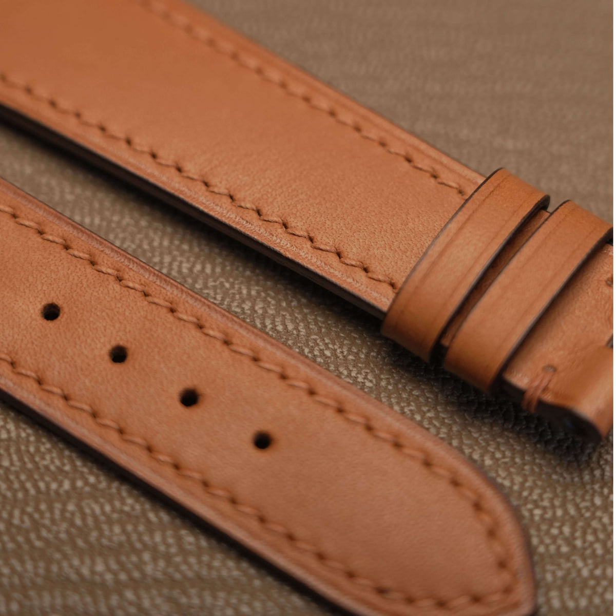 Macro detail of precision linear machine stitching and sealed edge finish on light brown calfskin watch strap