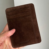 Brown suede leather wallet held in a hand against a white background