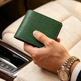 Hand holding a EPI leather green wallet with a gold watch on a car seat