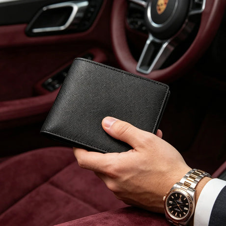 Hand holding a black saffiano wallet with a car interior background