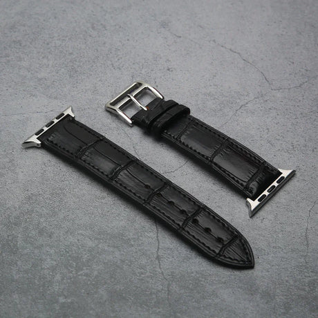 Black aligator leather watch strap with silver buckle on a gray concrete surface