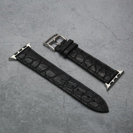 Black aligator leather watch strap with silver buckle on a gray surface