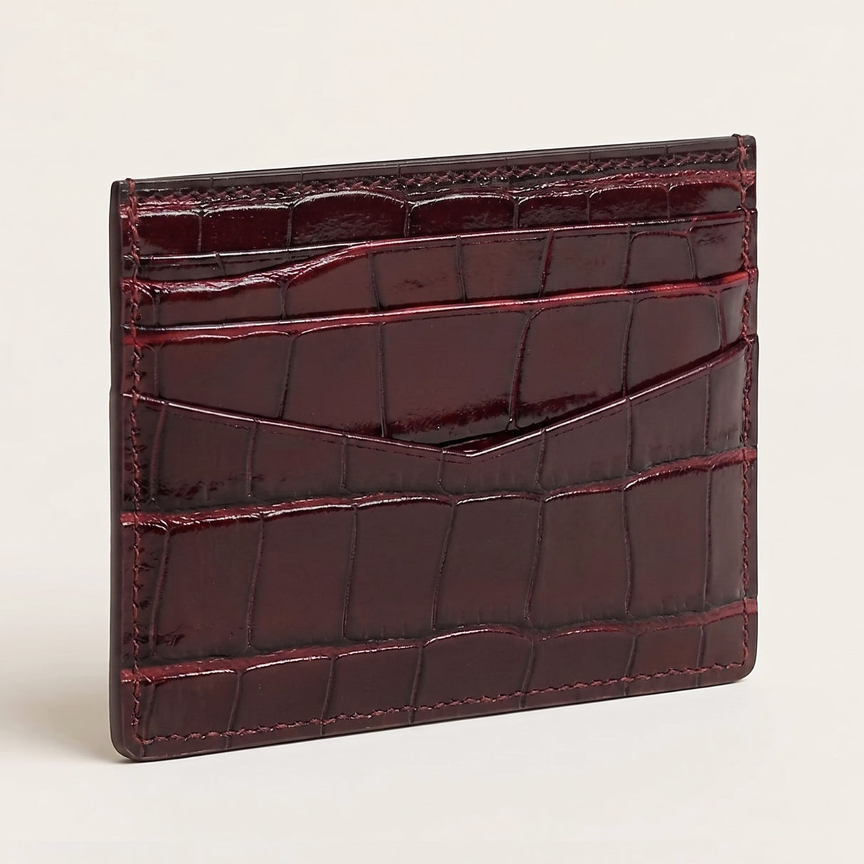A glossy crocodile-embossed card holder wallet in deep burgundy, shown standing upright on a light beige background.