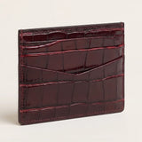 A glossy crocodile-embossed card holder wallet in deep burgundy, shown standing upright on a light beige background.
