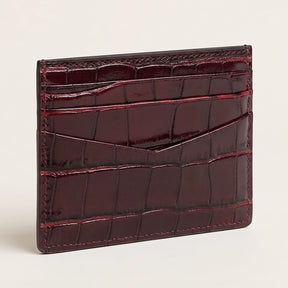 A glossy crocodile-embossed card holder wallet in deep burgundy, shown standing upright on a light beige background.
