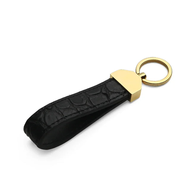 Matt black crocodile skin key fob with a gold accent on a white background