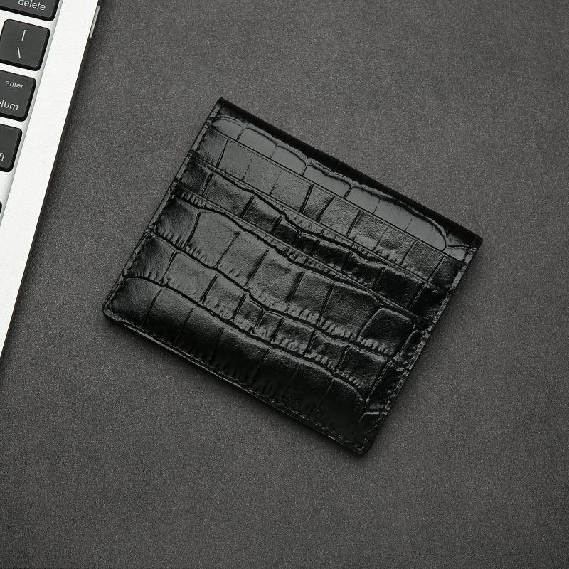 Black aligator-patterned wallet on a gray surface with a keyboard in the corner.