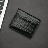 Black aligator-patterned wallet on a gray surface with a keyboard in the corner.