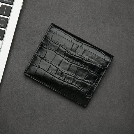 Black aligator-patterned wallet on a gray surface with a keyboard in the corner.