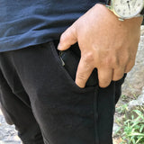 Person wearing black pants with a hand holding a pouch pouch, outdoors.