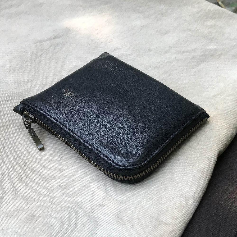 Black leather zippered coin pouch on a light gray fabric background