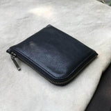 Black leather zippered coin pouch on a light gray fabric background