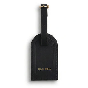 Black leather luggage tag with 'Hiram Beron' branding on a white background