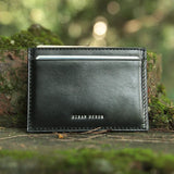 Black leather card holder with 'Hiram Beron' branding on a natural background