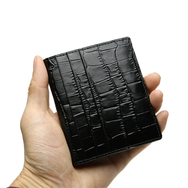 Hand holding a black aligator pattern wallet against a white background