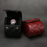 Black and red leather watch roll case with a watch inside on a gray background