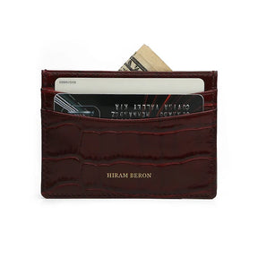 Slim Burgundy crocodile-patterned calfskin cardholder with cards and money on a white background