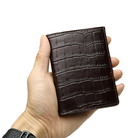 Hand holding a brown aligator-patterned wallet against a white background