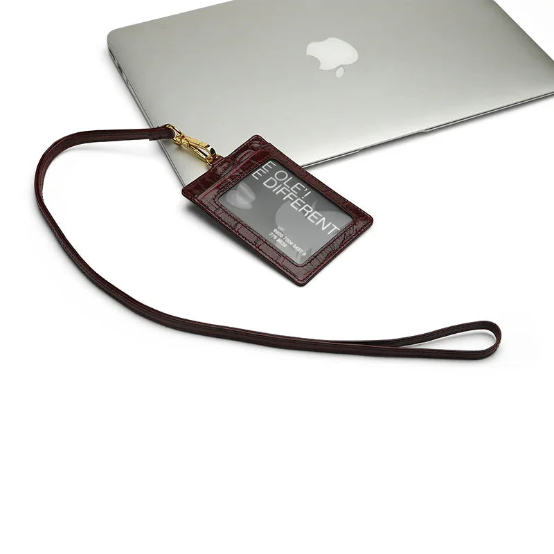 Burgundy leather ID badge holder with lanyard on a white surface with an Apple laptop in the background.