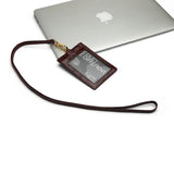 Burgundy leather ID badge holder with lanyard on a white surface with an Apple laptop in the background.