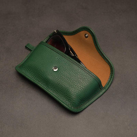 Green leather sunglasses pouch with a brown interior on a gray background