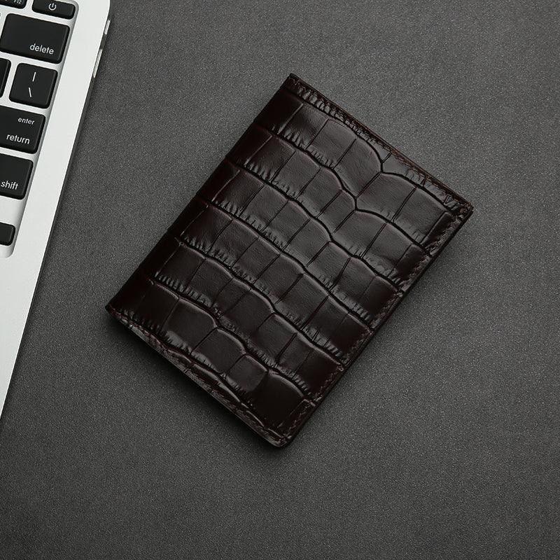 Brown aligator-patterned leather wallet on a gray surface with a keyboard in the corner.