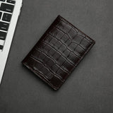 Brown aligator-patterned leather wallet on a gray surface with a keyboard in the corner.
