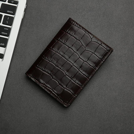 Brown aligator-patterned leather wallet on a gray surface with a keyboard in the corner.