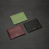 Three leather card holders in green, brown, and black on a dark gray background.