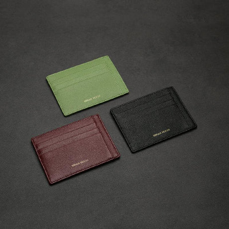 Three leather card holders in green, brown, and black on a dark gray background.