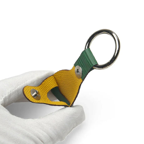Yellow and green leather keychain with metal ring, held in white glove