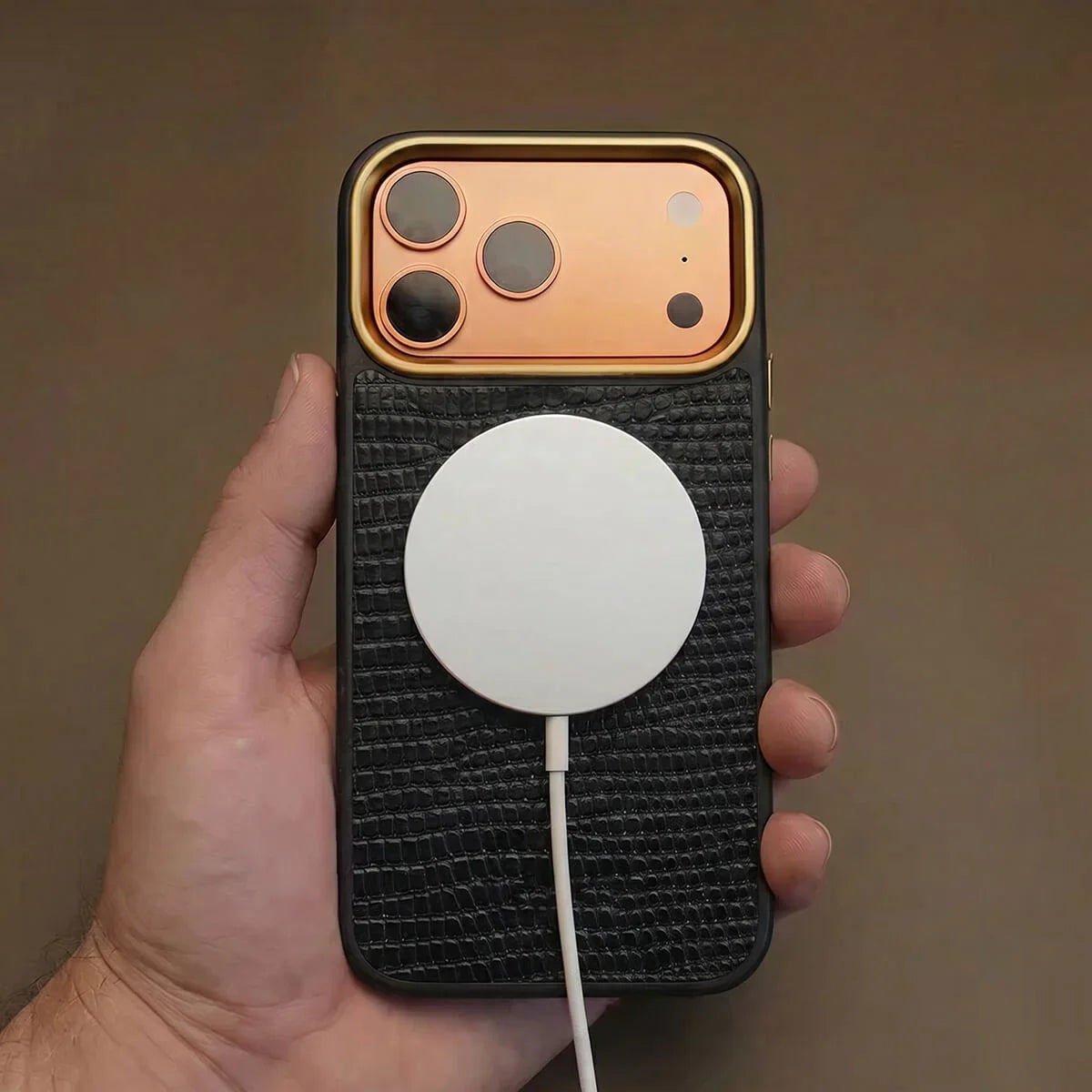 Hand holding an iphone with a black case and white cable against a brown background