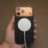 Hand holding an iphone with a black case and white cable against a brown background