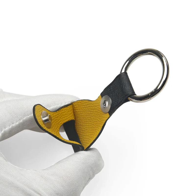 Leather Airtag Keychain holder with yellow and black design held by a white gloved hand on a white background
