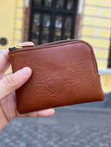 Brown vegetable tanned leather coin pcouh held in a hand with a blurred background